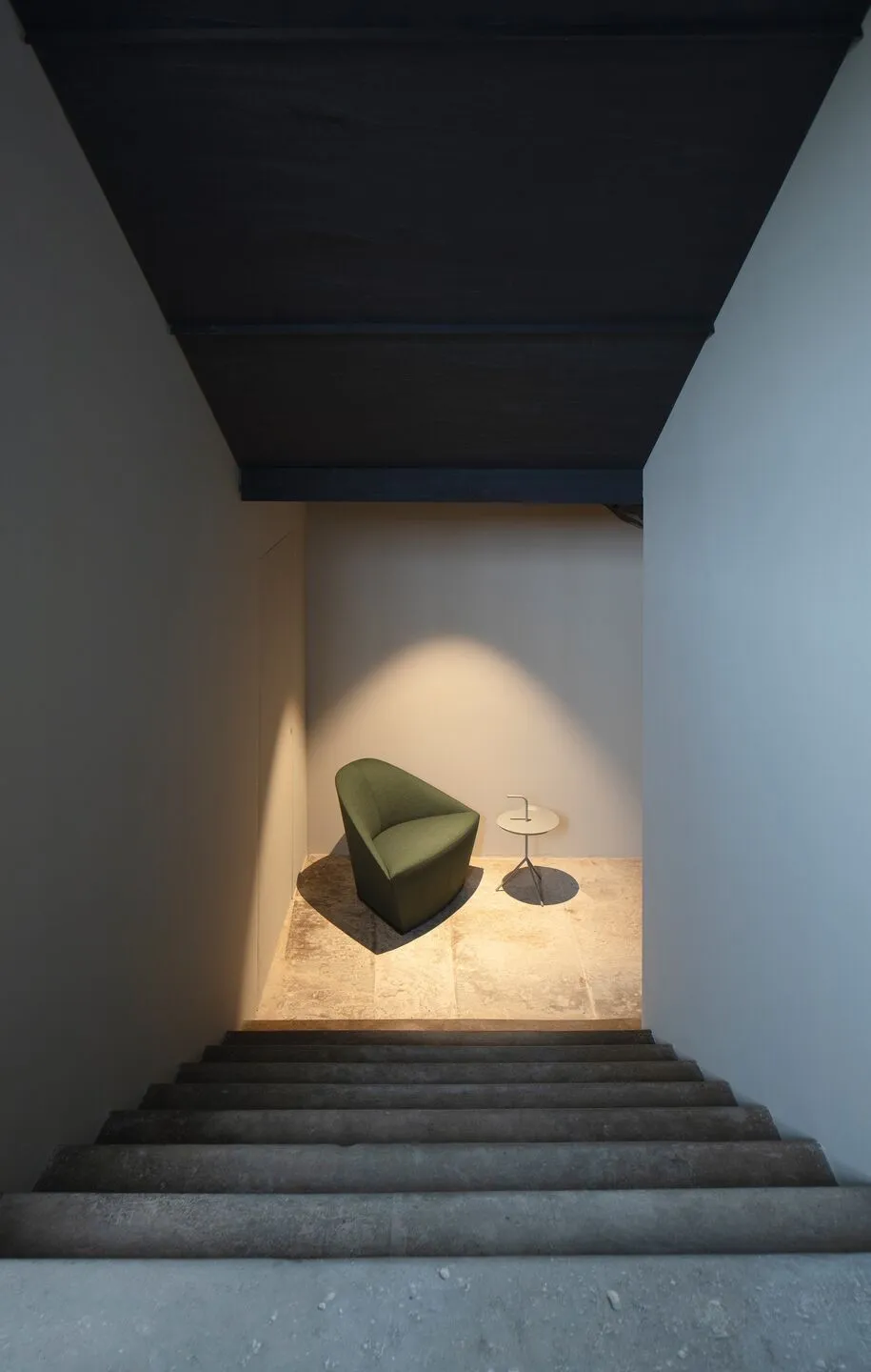 Minimalist interior space featuring a concrete staircase with a single green armchair and a small table.