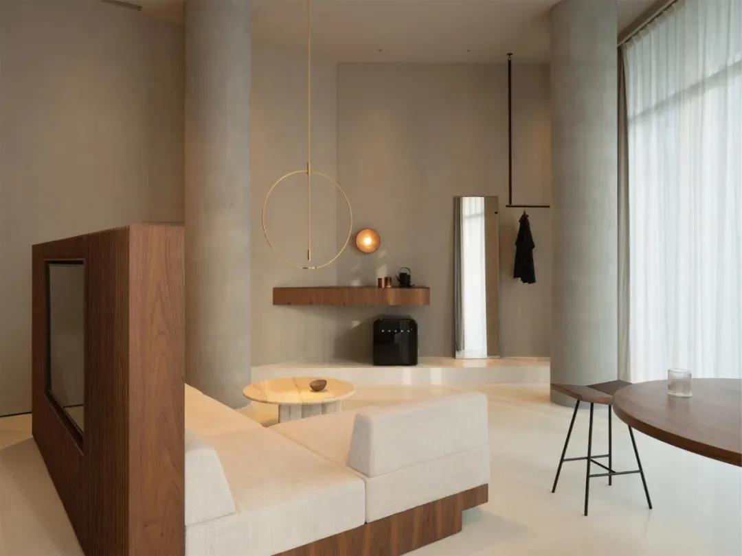 A modern minimalist living room featuring a white sofa with wood accents, a round wooden table, and a wooden divider with a m
