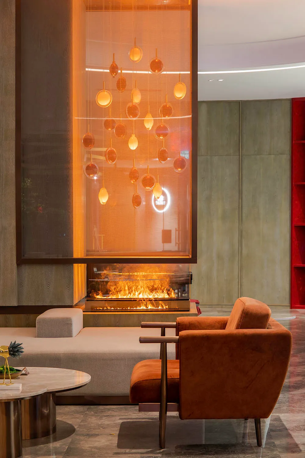 A modern office seating area with fabric chairs, a glass fireplace, and a hanging light fixture.