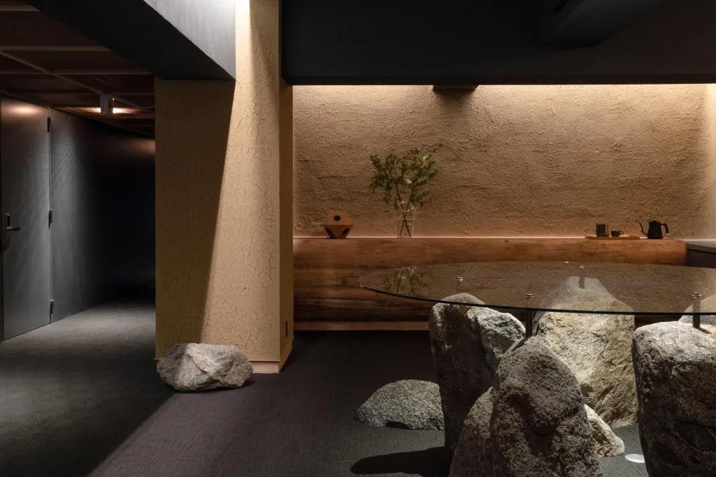 現代餐廳室內空間,混凝土牆面點綴岩石元素,搭配玻璃餐桌與自然岩石及花瓶