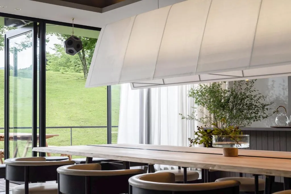 Modern, spacious restaurant interior with large windows showcasing a serene outdoor view, featuring minimalist design, white 