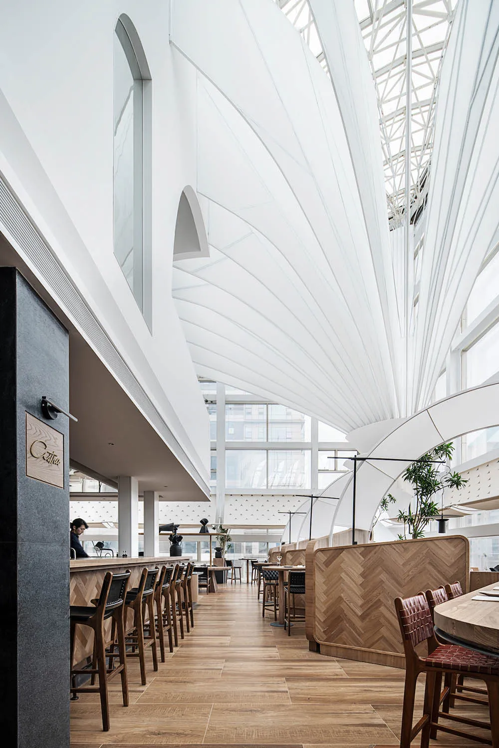 Modern restaurant interior with wooden tables, metal stools, and glass windows.