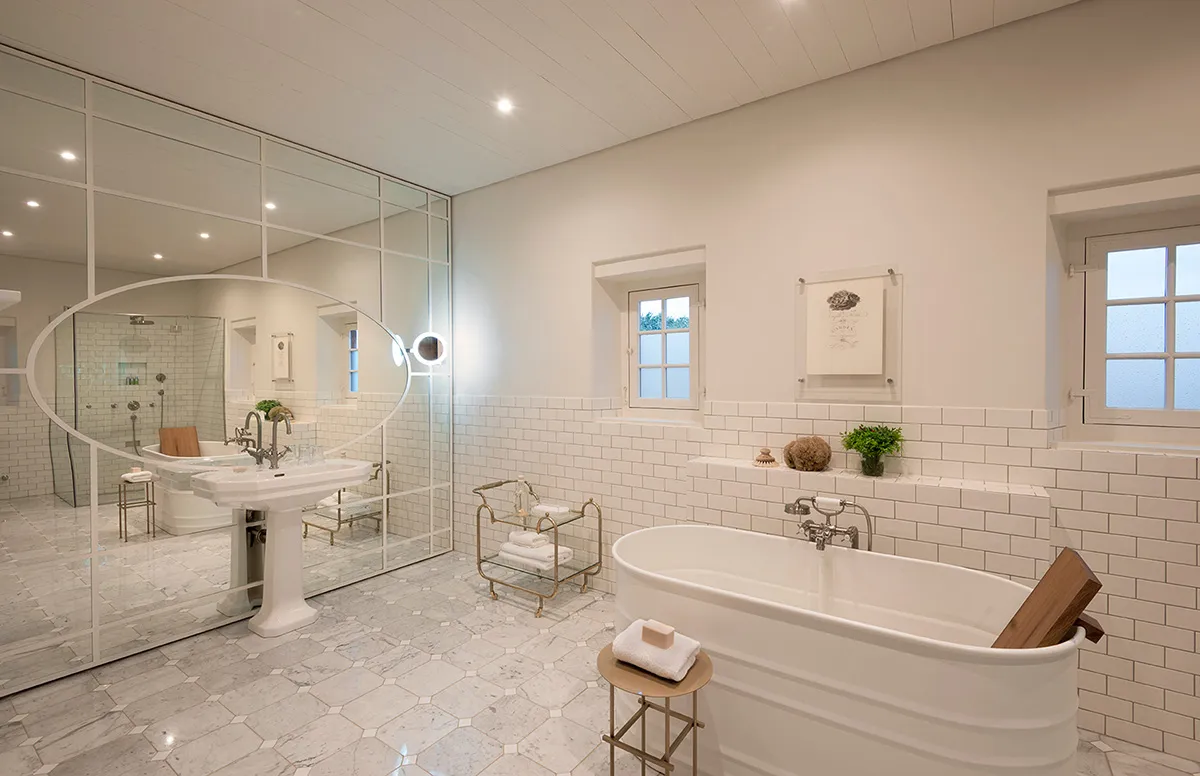 A modern, minimalist bathroom with white subway tiles, a freestanding bathtub, a pedestal sink, and a mirror.