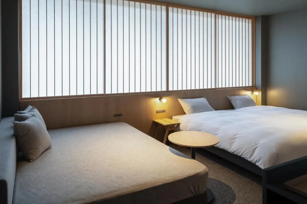 A modern minimalist bedroom featuring soft furnishings and a large window with light filtering shades.
