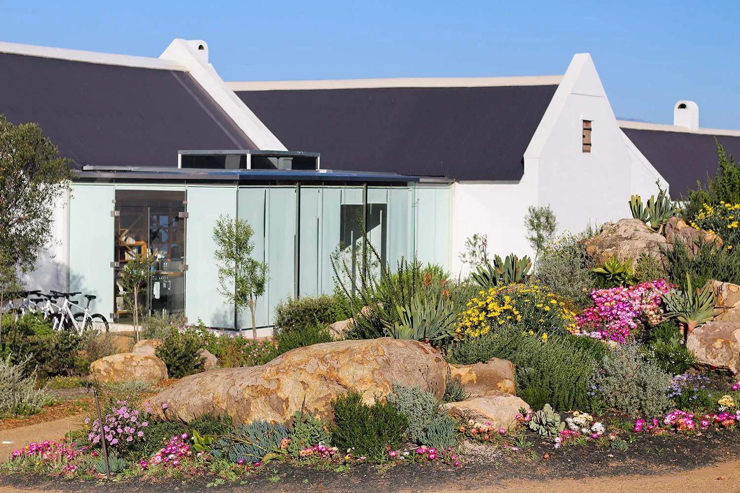 A modern building with black roof surrounded by greenery and rocks.
