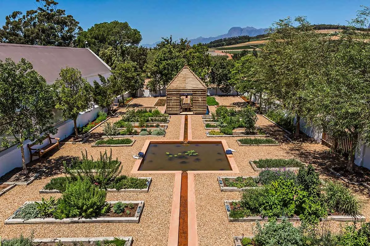 一座採用天然材質打造的現代花園,中央設有水景,周圍環繞著高架花壇。