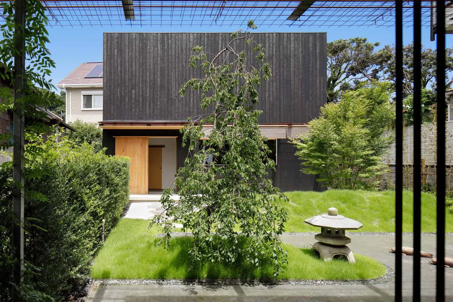A modern residential home with wooden exterior and large trees in the foreground.