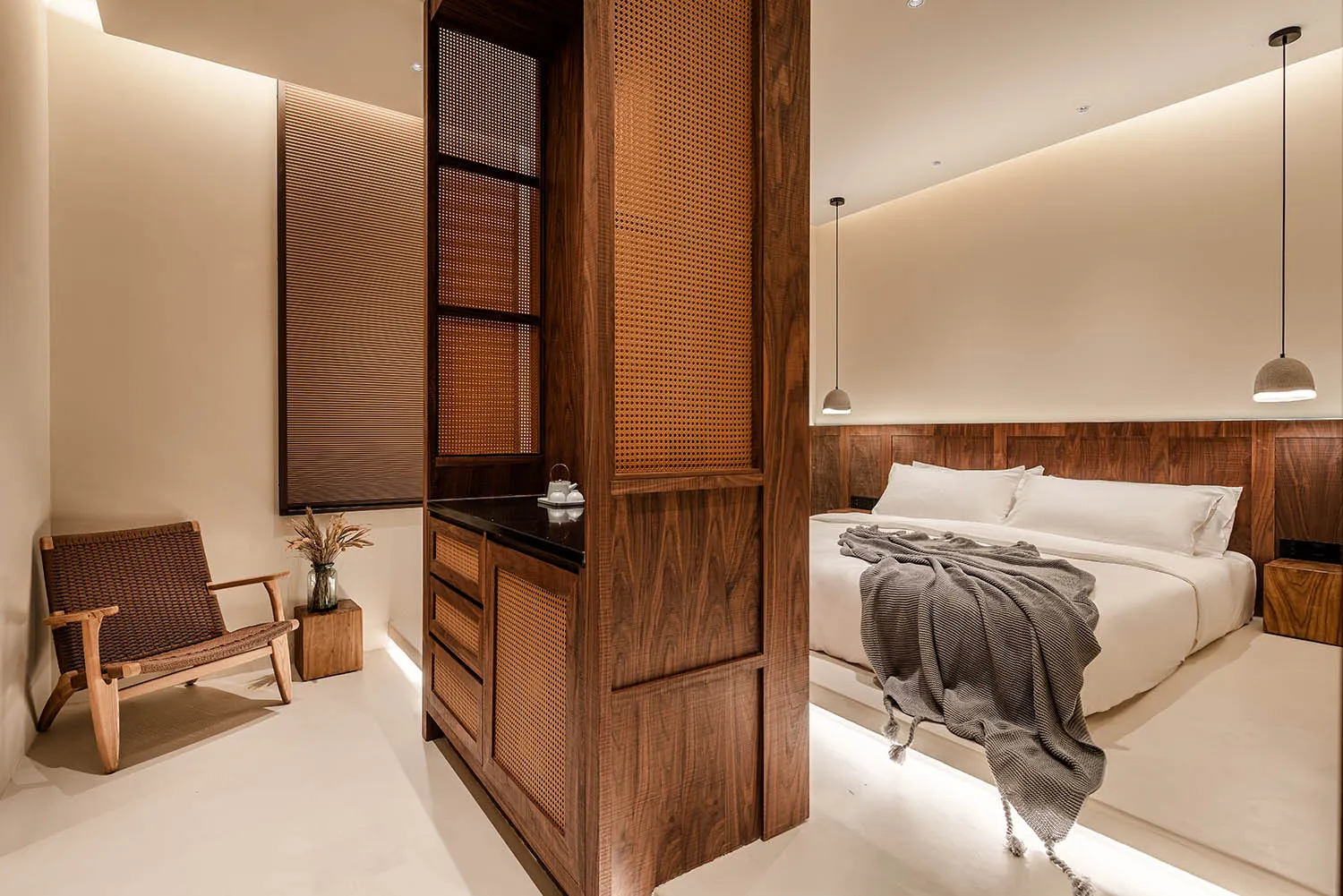 A minimalist bedroom featuring white walls and a wooden bed frame with a grey blanket draped over it.