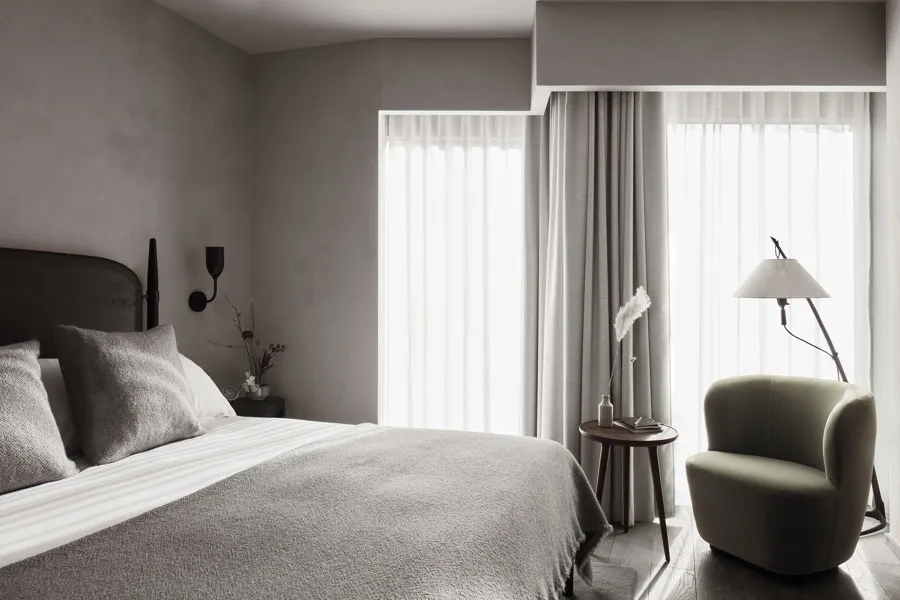 A minimalist bedroom with a bed, white curtains, and a green armchair.