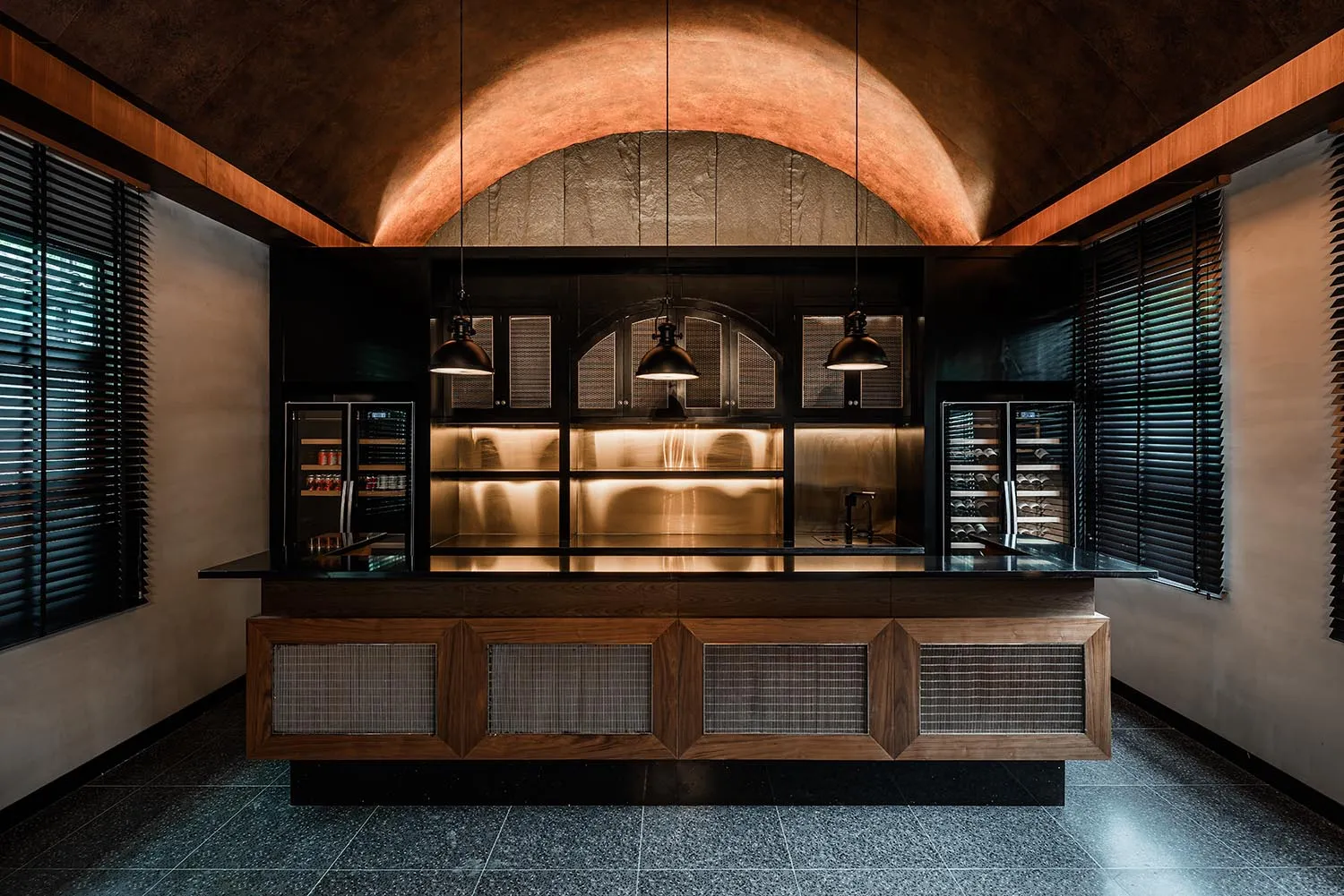 A sleek, modern kitchen with metallic finishes and industrial lighting features a bar area with a high ceiling and arched lig