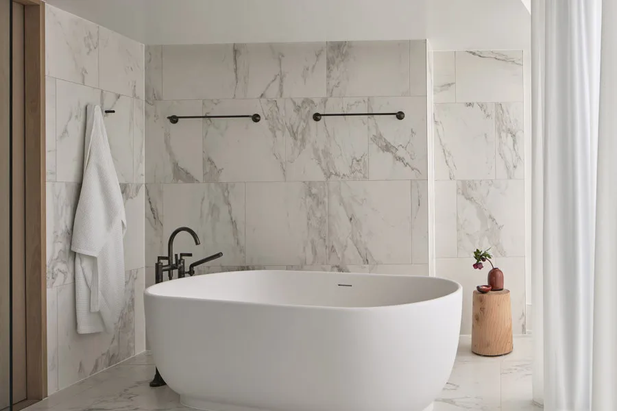A modern minimalist bathroom with a freestanding bathtub, black faucet, and marble tiles.