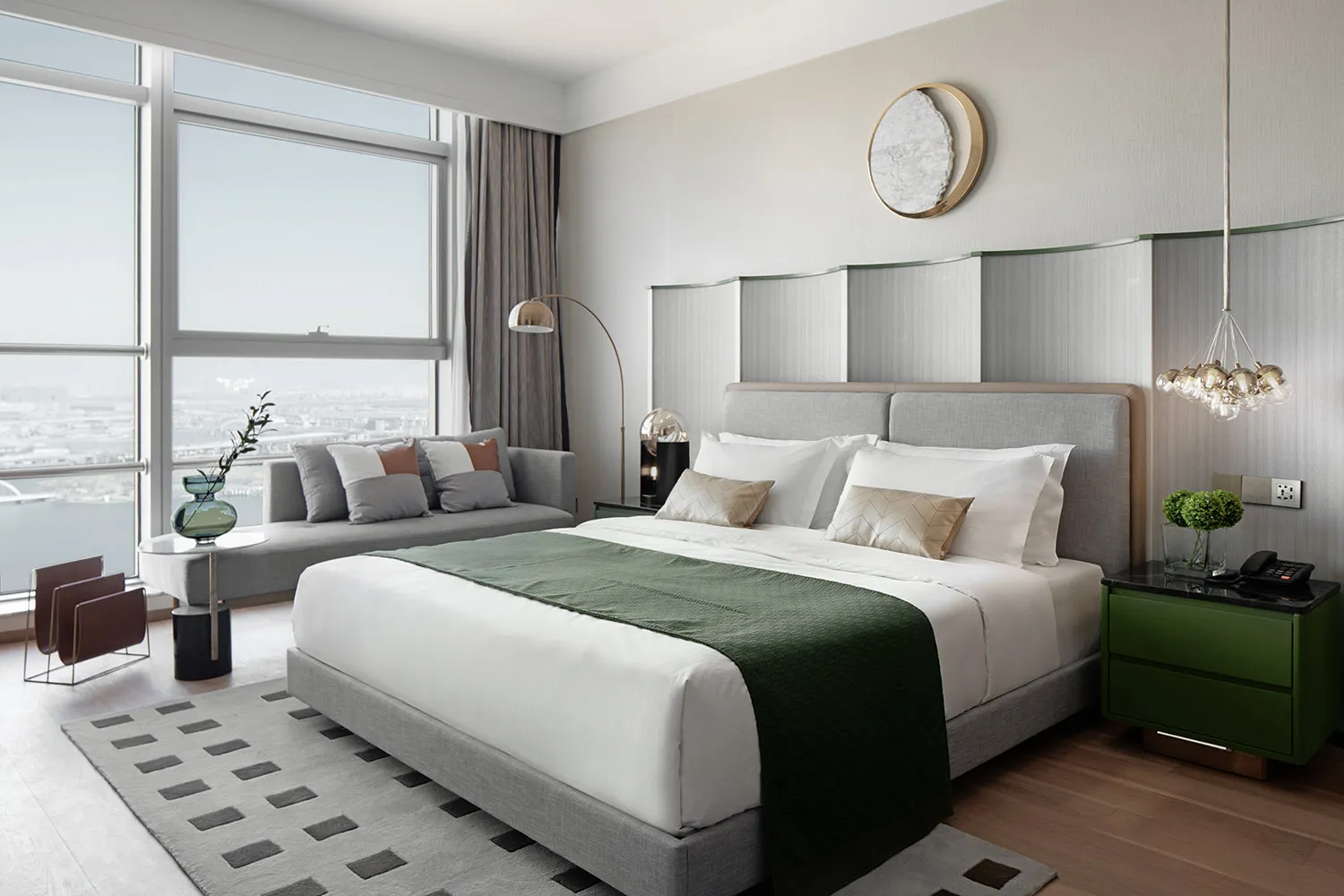 A modern minimalist bedroom with a gray bed, white linens, and a green throw blanket.