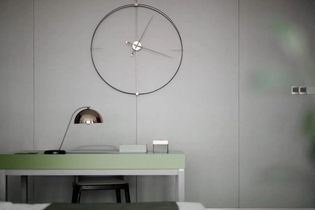 Circular modern metallic desk clock hanging above minimalist workspace with green desk and white chair.