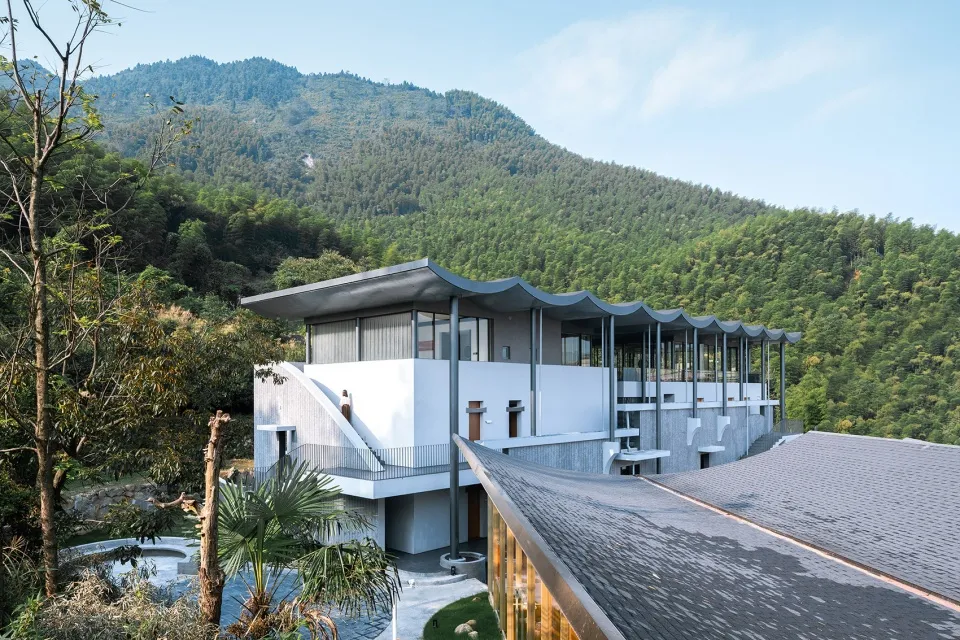 A modern residential building with concrete, glass, and wood exterior materials, surrounded by nature.