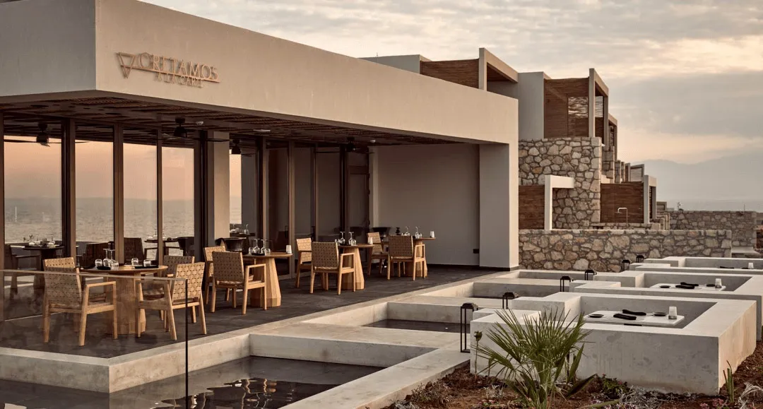 Modern restaurant exterior with glass walls, concrete ground, and wooden furniture.