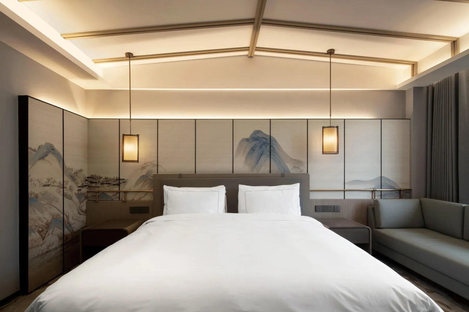 A modern minimalist bedroom featuring a large bed with white bedding, a grey sofa, and a wall with traditional Chinese artwor
