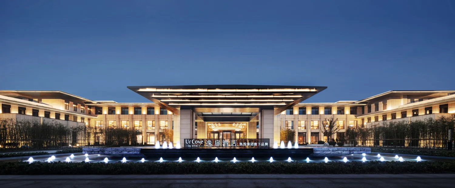 A modern hotel entrance with illuminated lighting, glass facade, and concrete pillars.