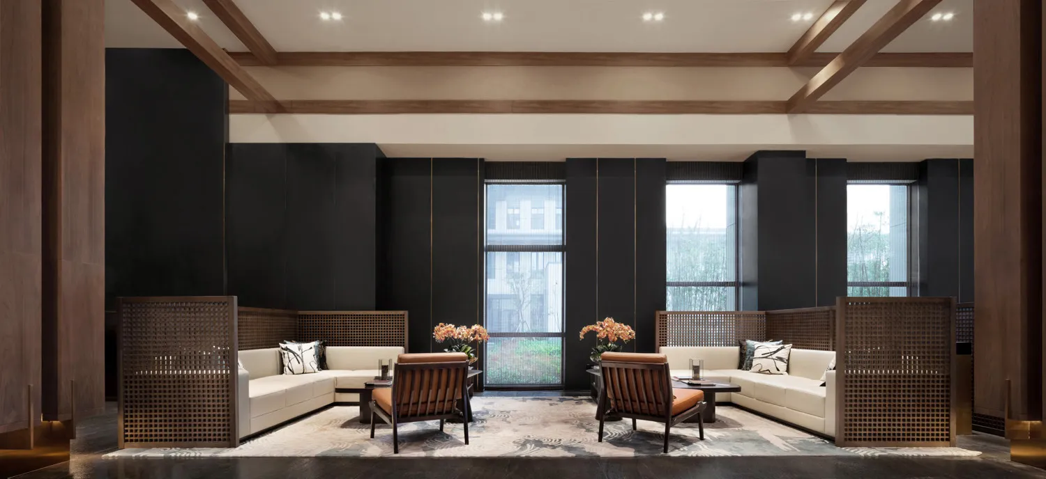 Modern living room featuring white sofas with orange cushions, wooden chairs, and a patterned rug with white walls and ceilin