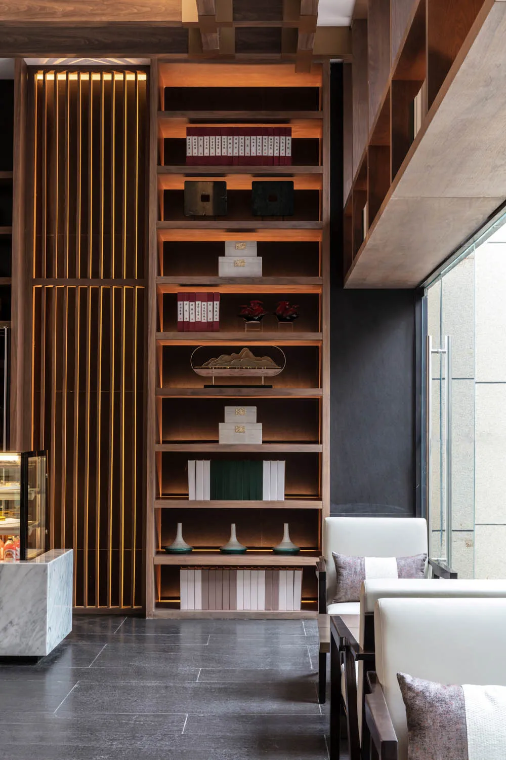 A modern lobby featuring a tall wooden bookshelf with various decorative items and books.