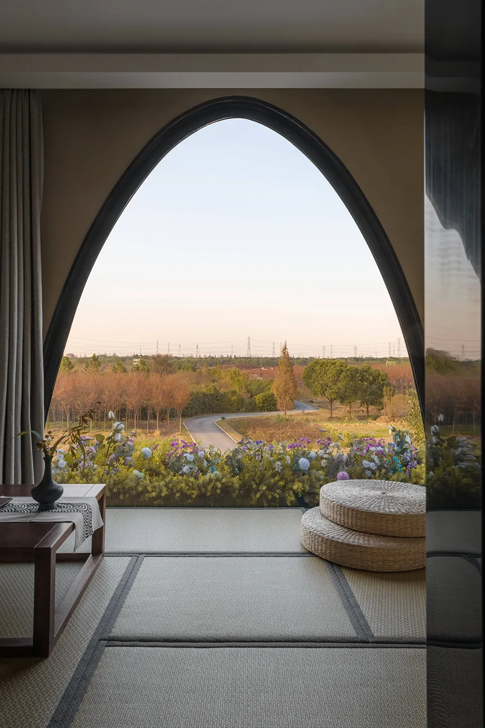 A living room interior framed by an arched window overlooking a serene outdoor landscape with wooden cushions on the floor, g