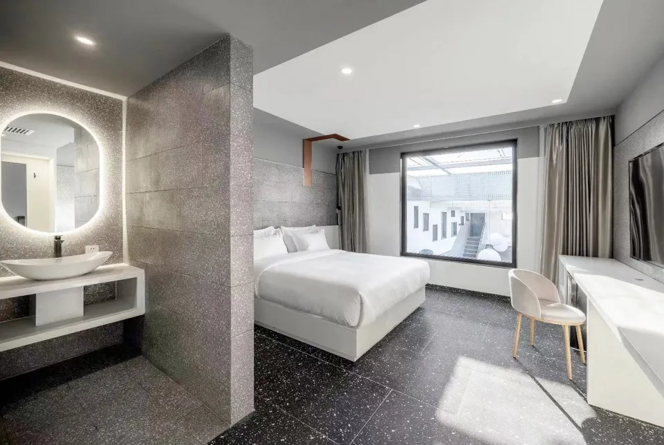 Modern, minimalist hotel room featuring glass walls, concrete flooring, and white textiles.