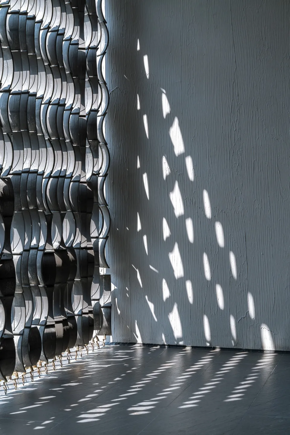 A minimalist interior design featuring metallic elements casting patterned shadows on the wall and floor.