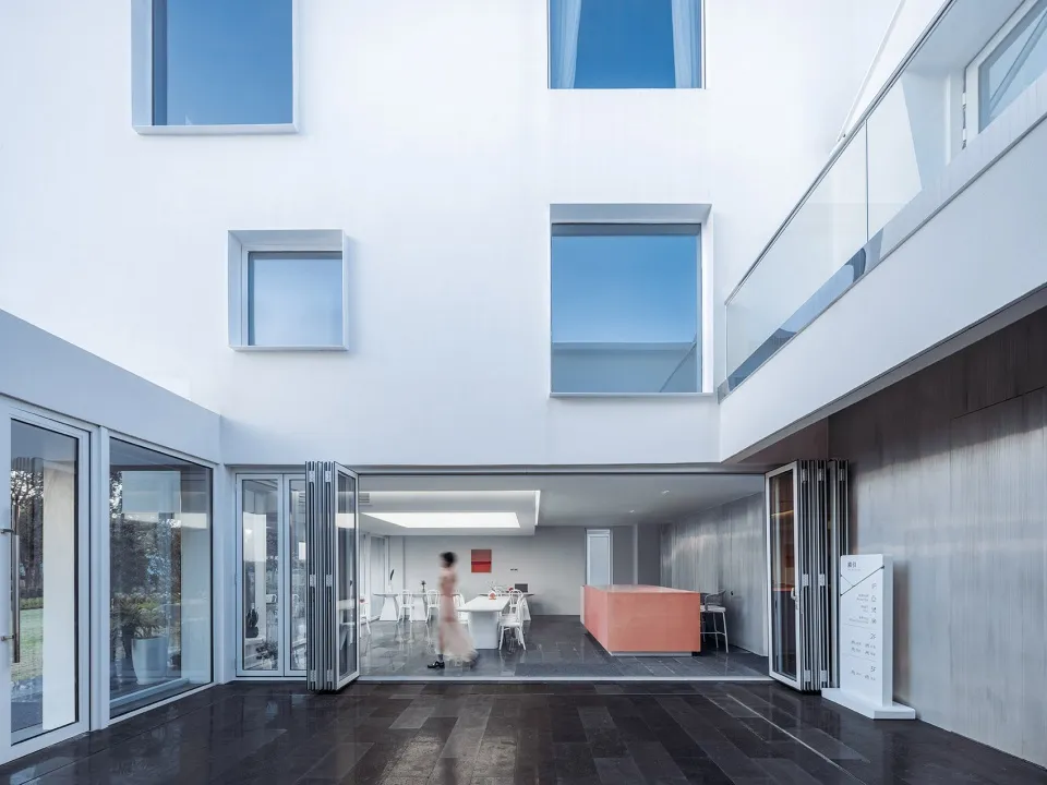 Modern living room with concrete walls, large floor-to-ceiling windows, and minimalist furniture.