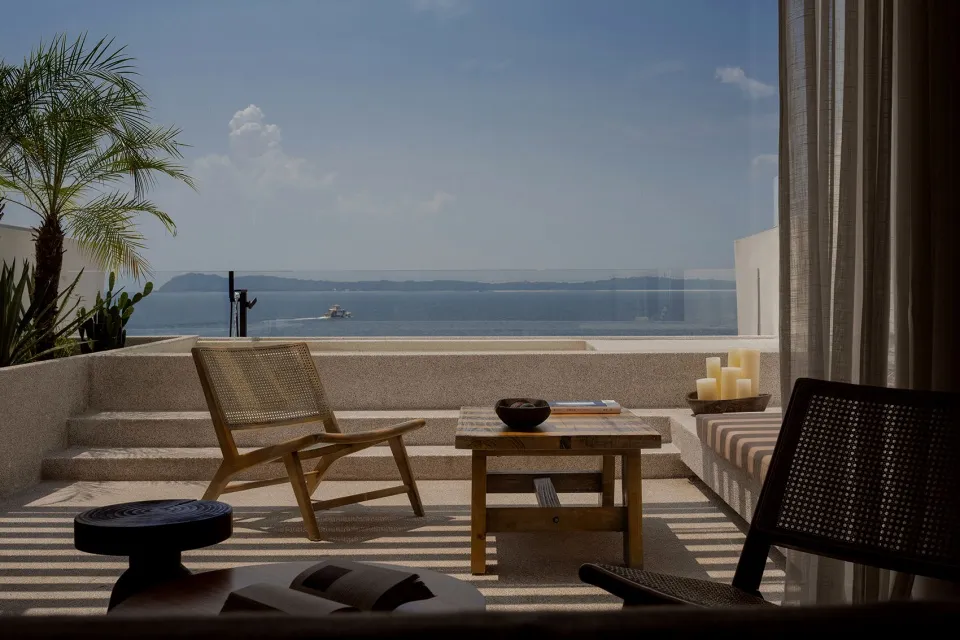 Modern patio with concrete floor, wooden furniture, and palm plants overlooking the ocean.