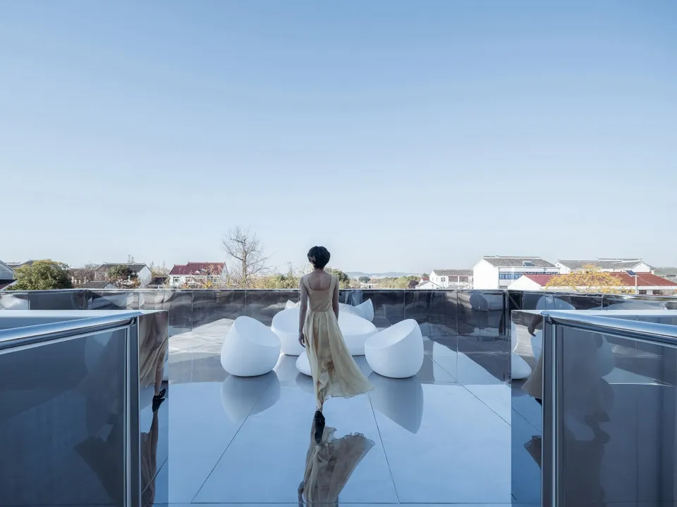 A modern rooftop space featuring glass furniture and a single individual.