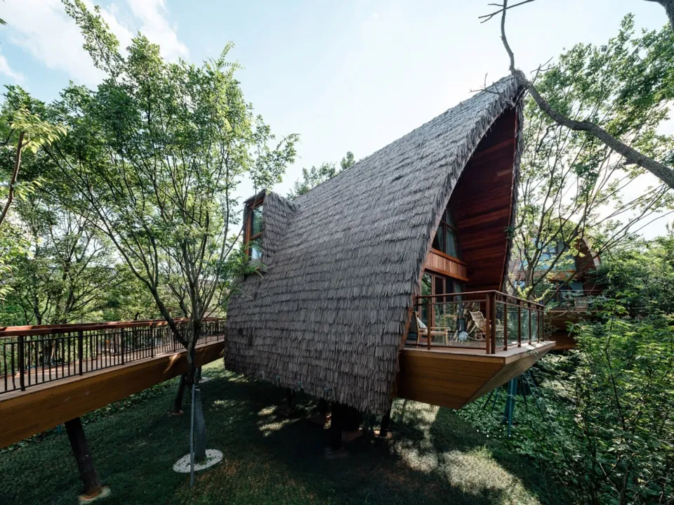 A wooden thatched roof treehouse nestled in a forest.