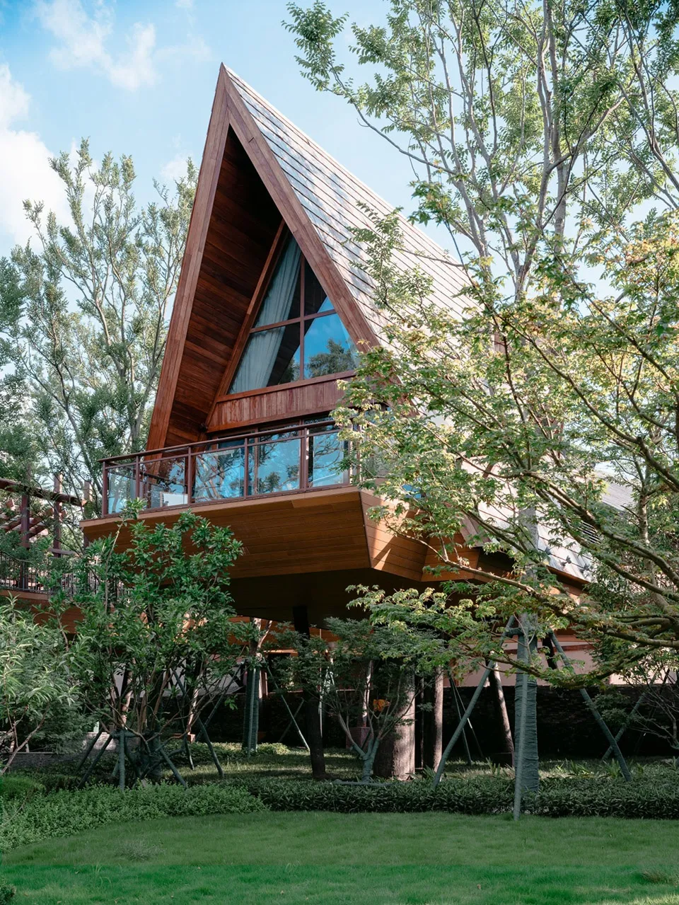 Modern residential home with wooden exterior and large windows surrounded by greenery.