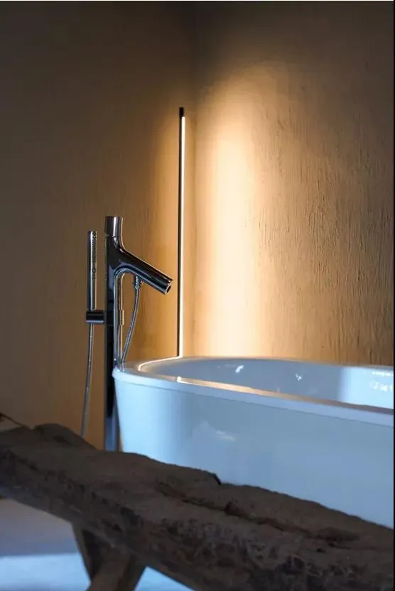 A simplistic bathroom featuring a sleek ceramic bathtub and a modern, minimalist sink faucet in a well-lit room.