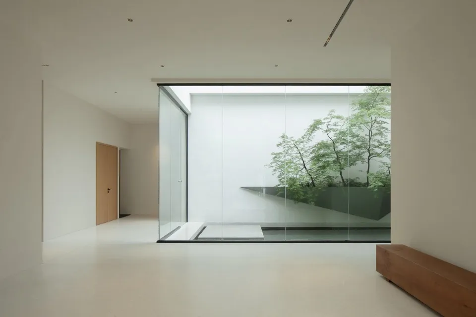 A minimalist interior space featuring large glass walls looking out onto a green courtyard.