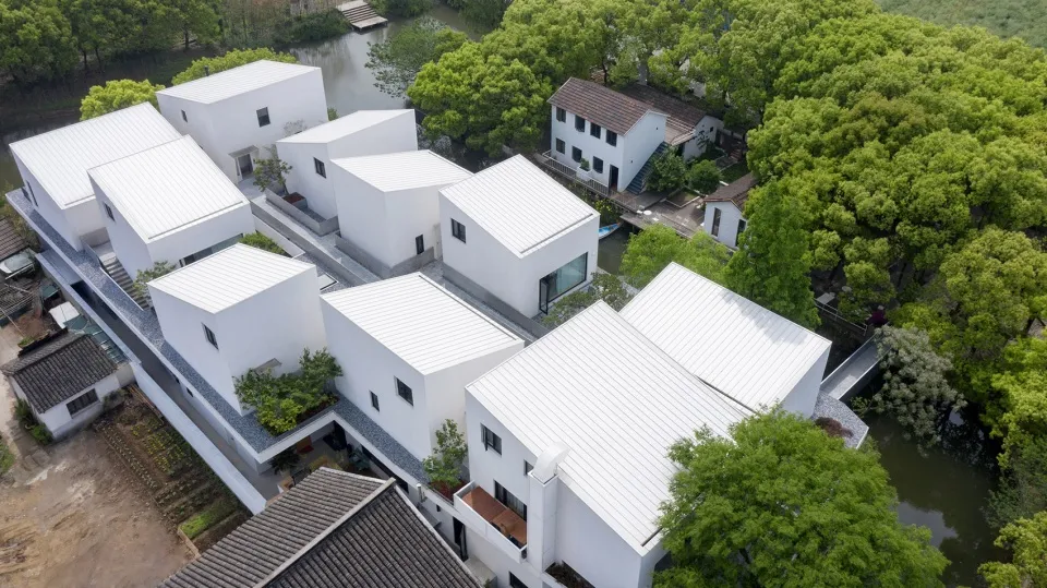 Aerial view of modern residential architecture with white metal roofing surrounded by green trees and water channels.