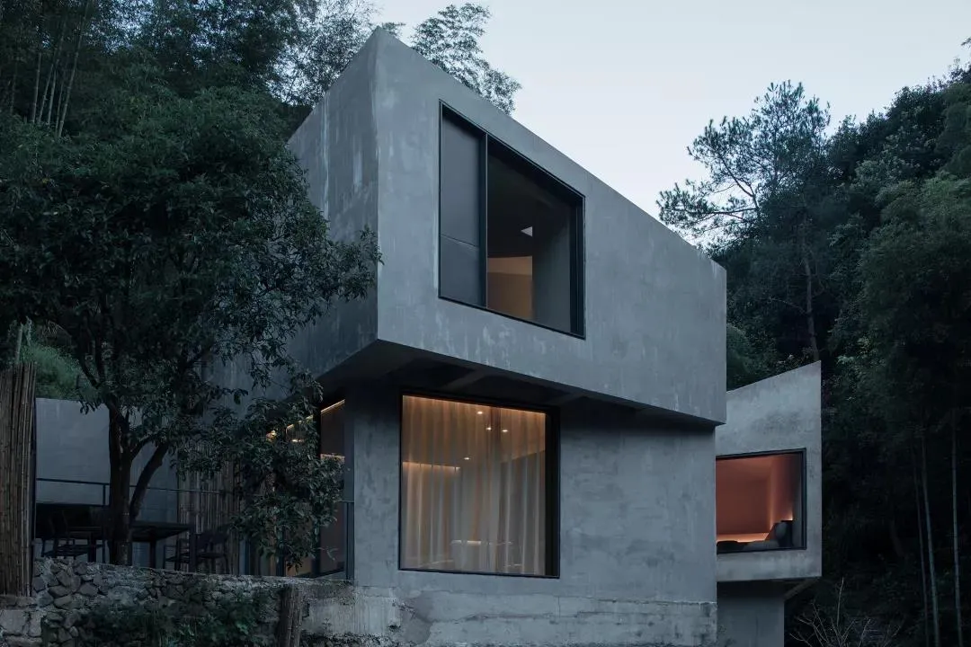Modern concrete residential interior with large windows and warm lighting.