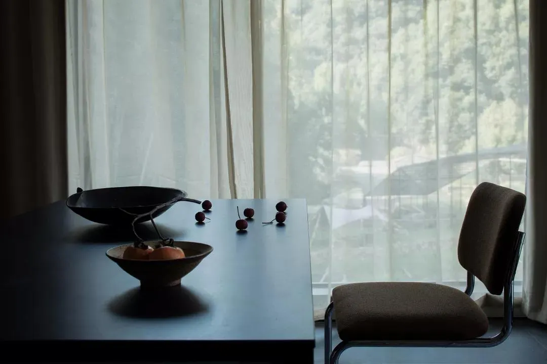 A photograph of a modern interior design featuring a window with a view of a serene landscape, a table with a bowl of fruit a