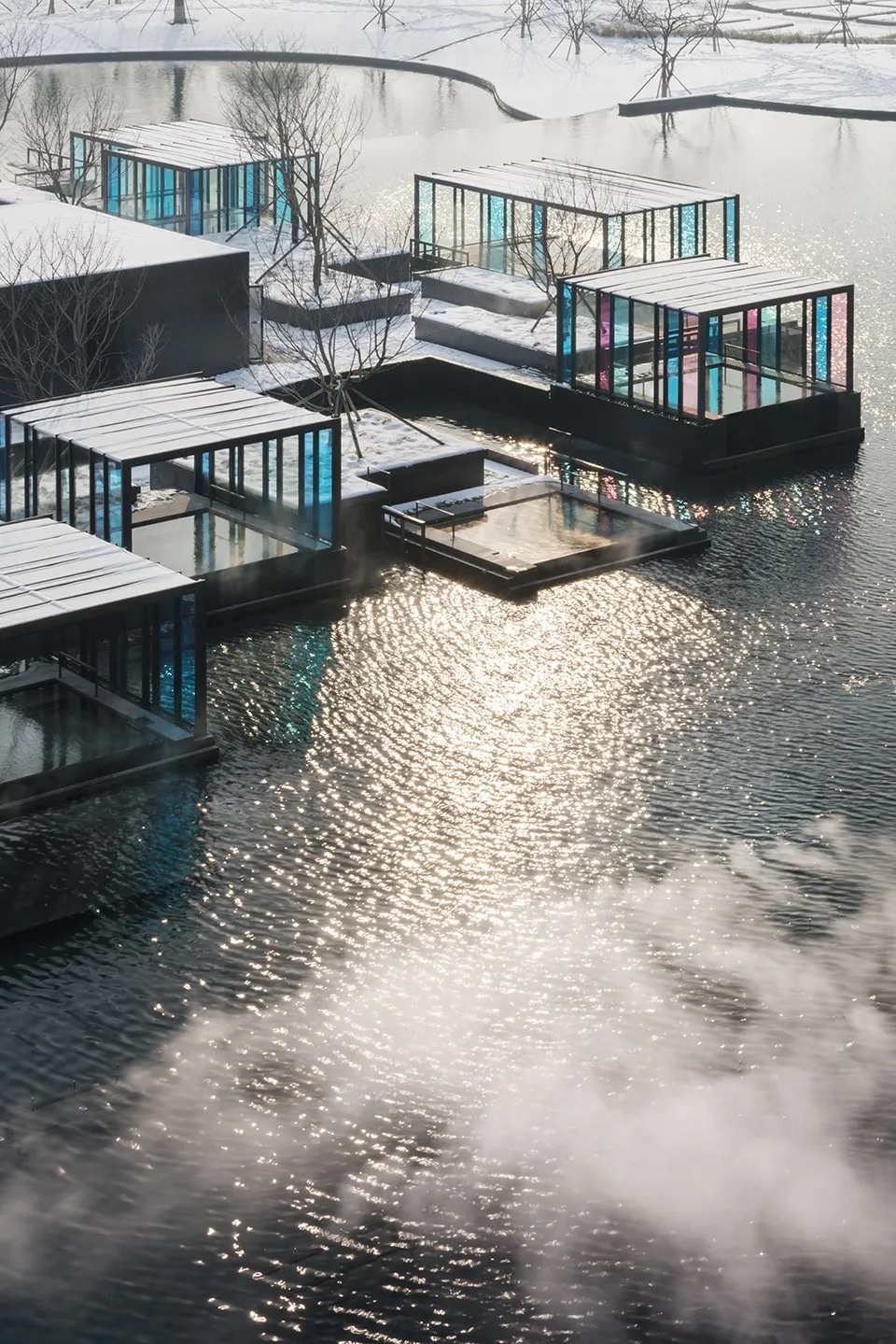 現代度假村以玻璃與混凝土結構坐落於雪景水域旁,呈現幾何建築設計。