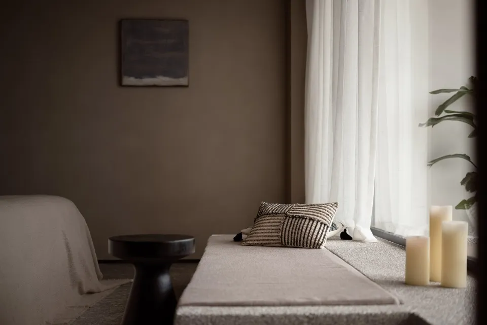 A minimalist bedroom featuring textured textiles on a window seat and a black stool.