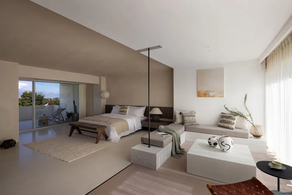 A minimalist bedroom with a white bed, neutral-colored walls, and modern furniture.