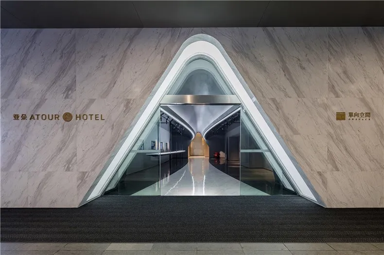Modern hotel entrance featuring marble walls, glass doors, and metallic accents.
