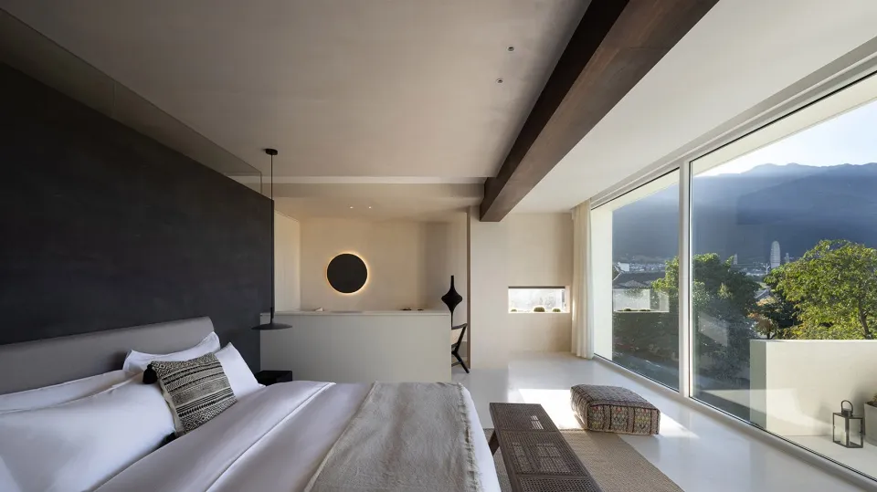 Modern minimalist bedroom featuring concrete flooring, white bedding, and a large window overlooking a scenic landscape.