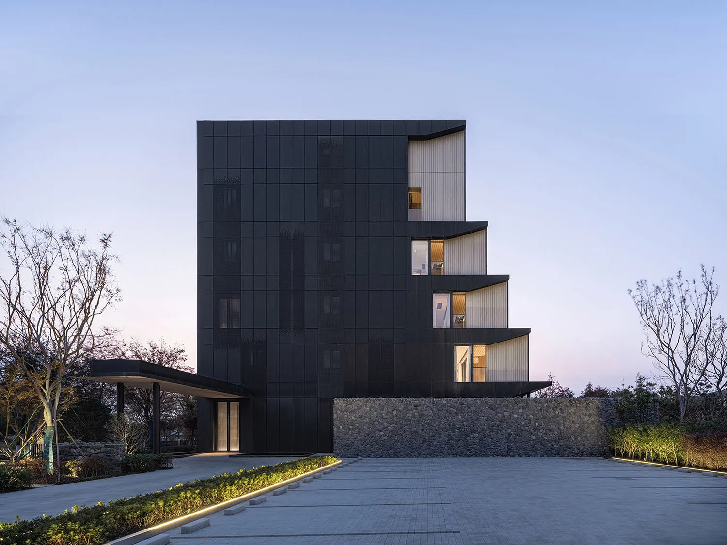 A modern office building with a black metal-clad exterior at dusk.