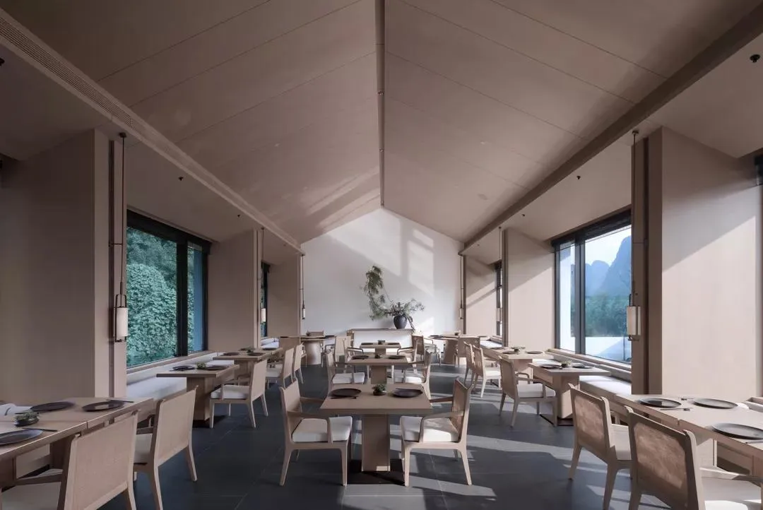 Modern restaurant interior with concrete finishes, white chairs, and large windows.