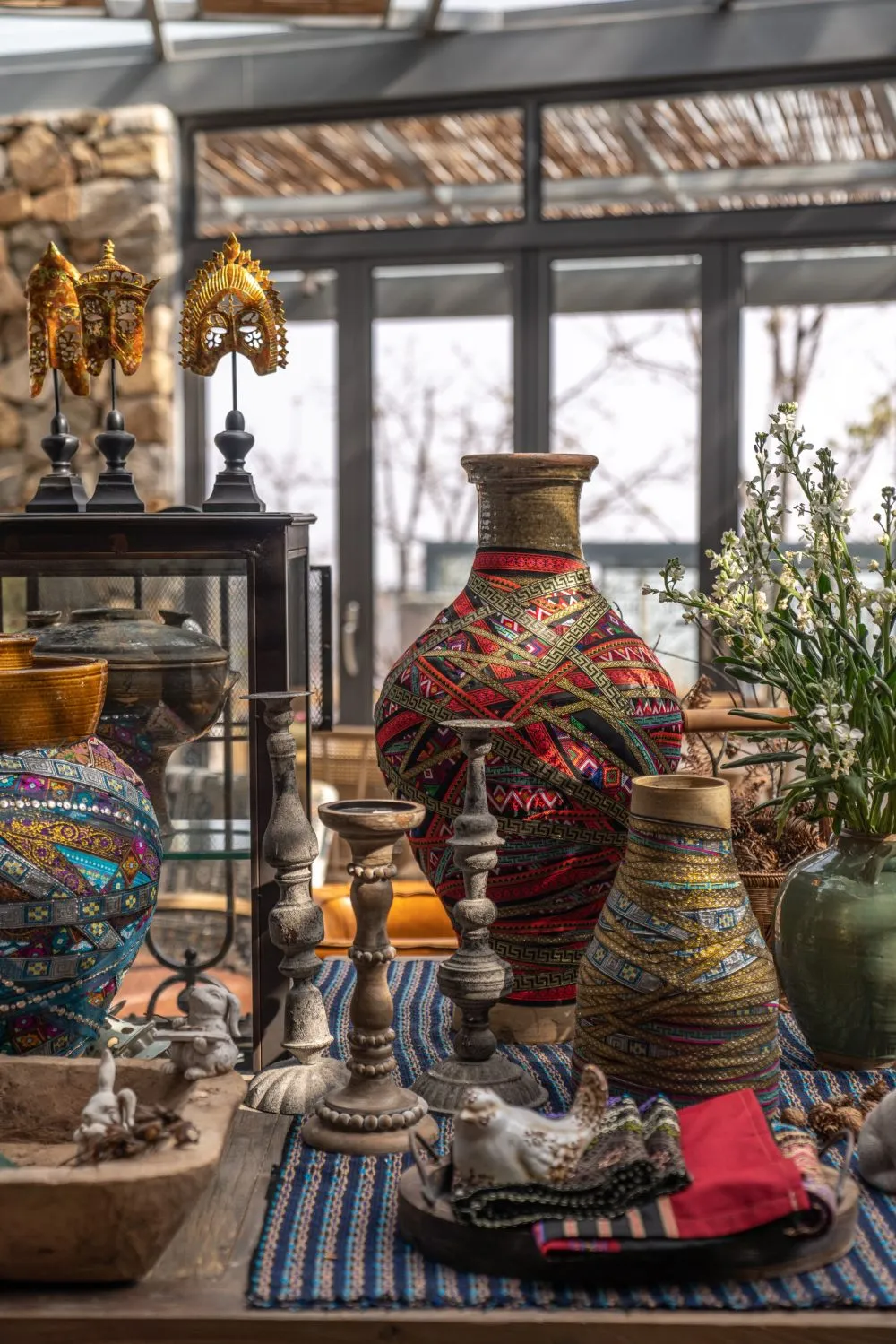 A variety of decorative objects placed on a table, including vases, candles, and plants, with a bohemian aesthetic.