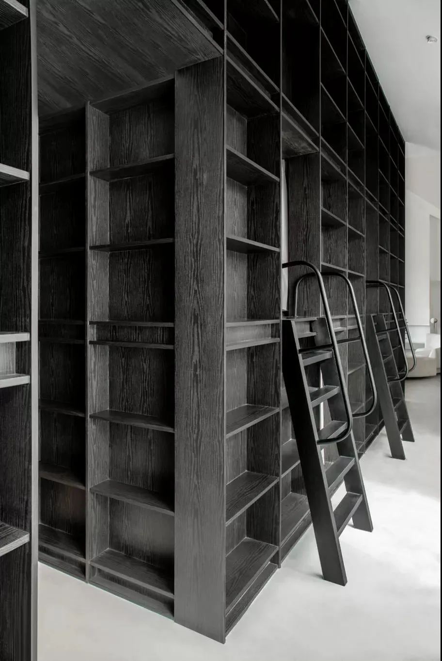 A spacious, minimalist dark wood library with built-in shelves and metal ladders.