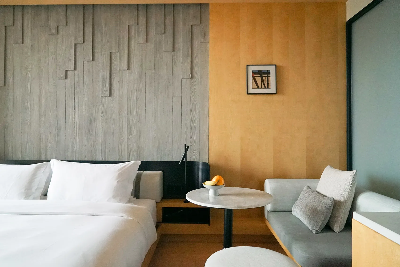 A minimalist residential room featuring white furniture, a wooden table, and a comfortable seating area.