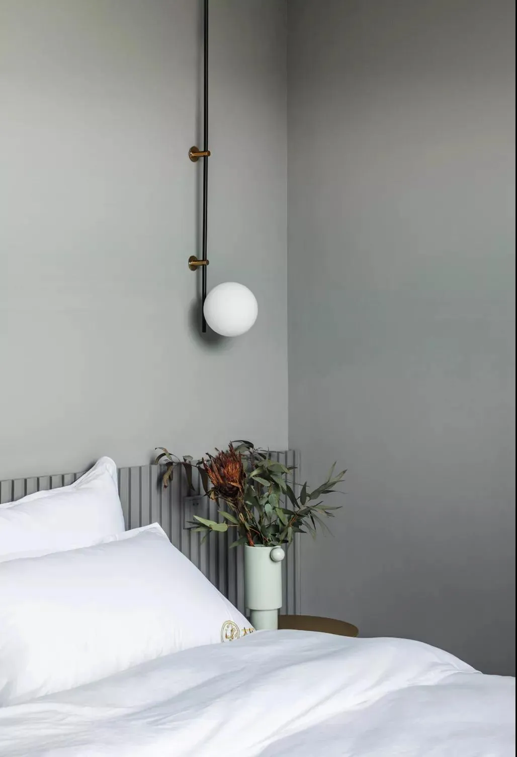 A minimalist bedroom with a white bed and hanging spherical light fixture.