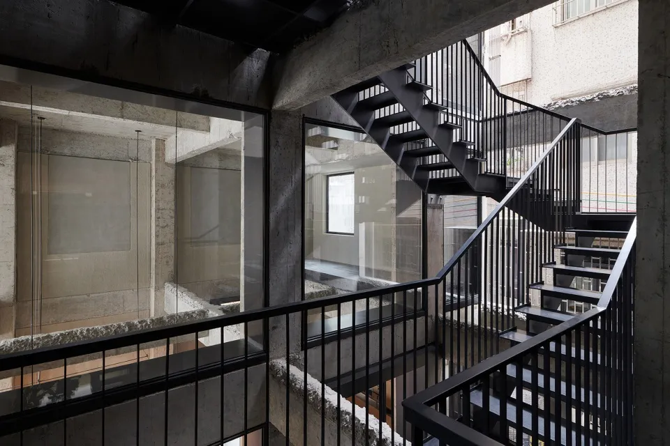 Black metal staircase with concrete walls and glass railings in an industrial-style interior.
