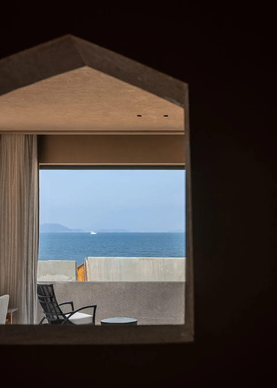 A balcony overlooking the ocean with concrete surfaces and a single white cushioned chair.