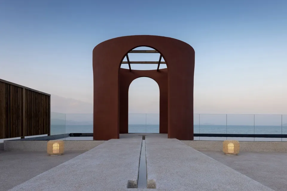 A minimalist red concrete architectural installation near the sea during dusk.